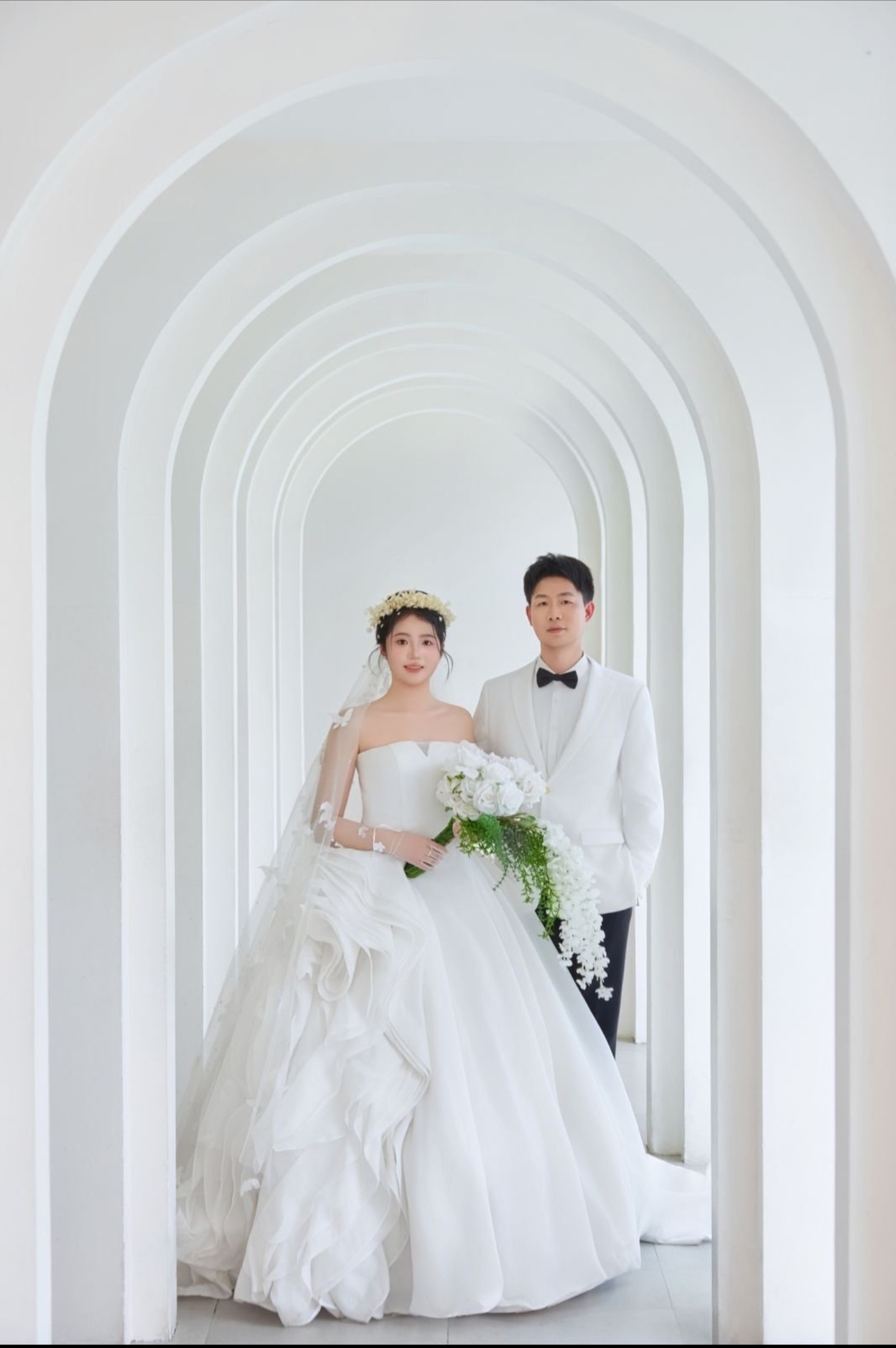 新人站在白色拱门下的婚纱照
